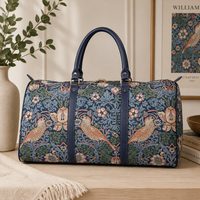 William Morris Strawberry Thief blue tapestry duffel bag with birds and floral pattern, navy faux leather handles, and spacious weekender holdall design for travel and overnight trips.