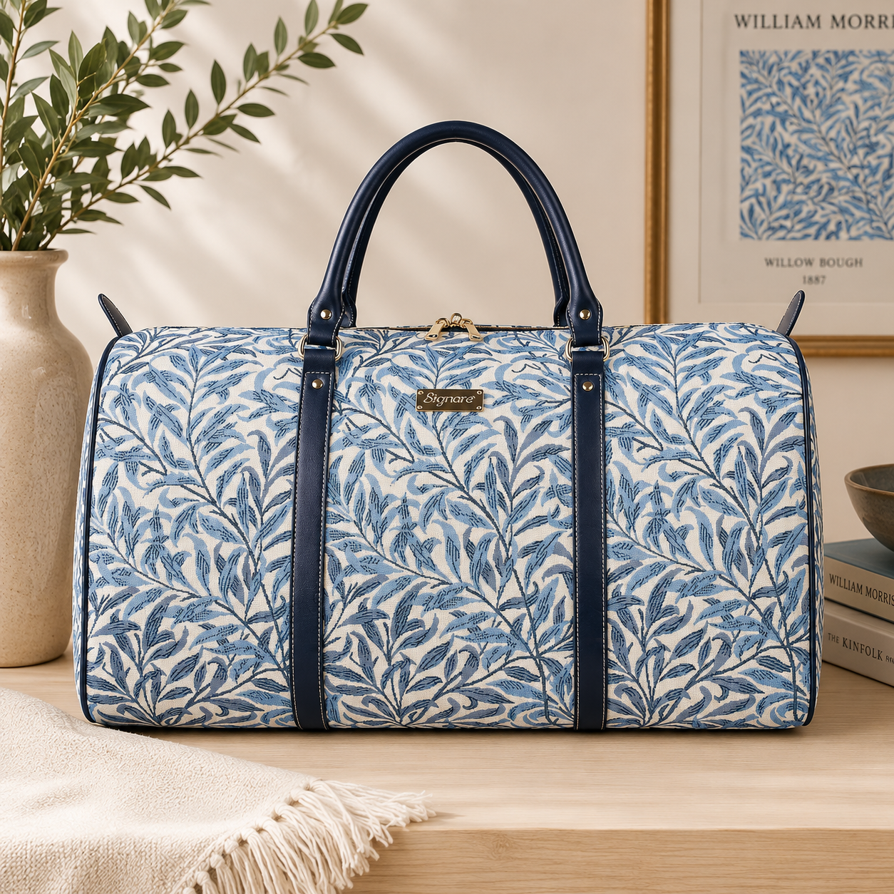 William Morris Willow Bough blue tapestry duffel bag with woven leaf pattern, navy faux leather handles, and spacious weekender holdall design for travel and overnight trips.